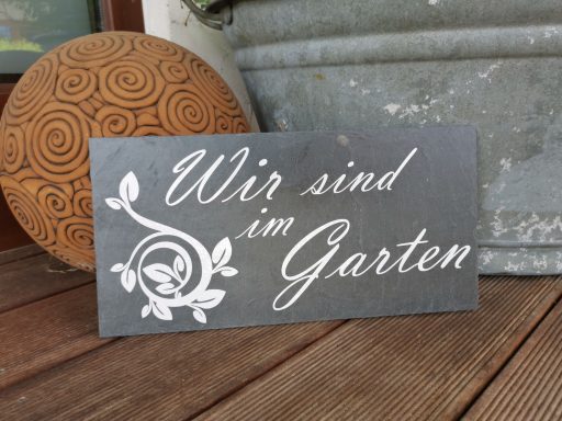 Schieferplatte mit der Aufschrift "Wir sind im Garten" und dekorativem Pflanzenmotiv.