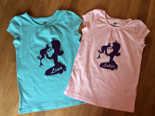 Zwei T-Shirts, eines aqua und eines rosa, mit einer Prinzessin-Figur aufgedruckt.