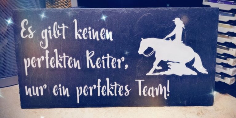 Text auf einer Tafel: „Es gibt keinen perfekten Reiter; nur ein perfektes Team!“ mit Pferdebild.