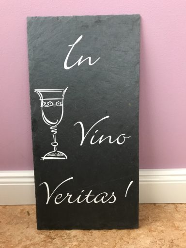 Schwarze Tafel mit der Aufschrift "In Vino Veritas!" und einem Weinglas-Symbol.
