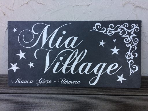 Schild mit der Aufschrift "Mia Village" und dekorativen Sternen und Mustern.