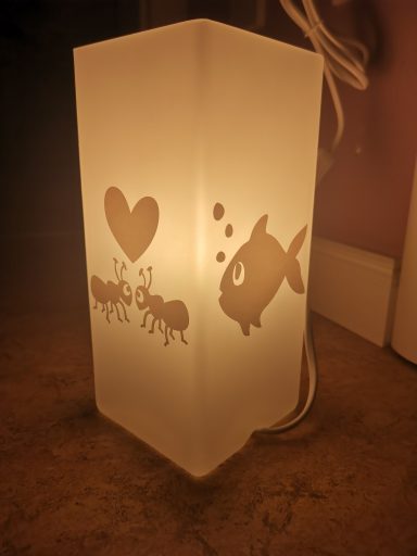 Eine beleuchtete Lampe mit Fisch- und Herzmotiven auf mattem Glas.